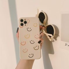 a person holding up a phone case with smiley faces on it and sunglasses hanging from the wall