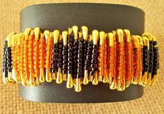 an orange and black beaded bracelet with gold accents on a black leather wristband