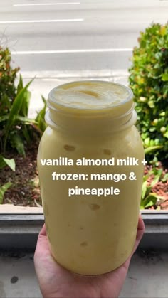 a hand holding a jar filled with vanilla almond milk and frozen mango & pineapple