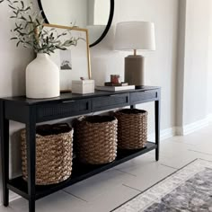 a black console table with baskets and a round mirror on the wall in front of it