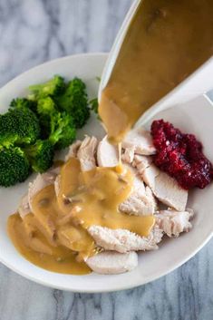 someone is pouring gravy on some chicken and broccoli with cranberry sauce