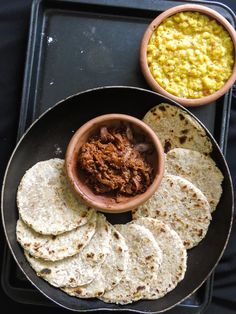 tortillas and salsa are served on a black tray with a bowl of beans