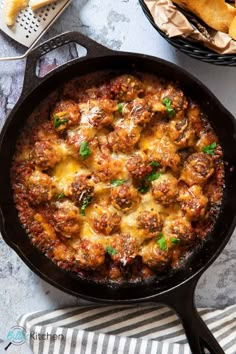 a skillet filled with meatballs and cheese on top of a table next to bread