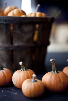 several small pumpkins sitting on a table next to a basket full of smaller ones