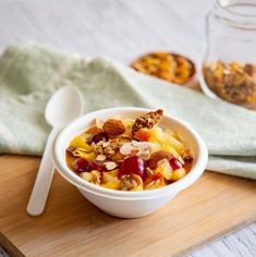 a bowl filled with fruit and nuts on top of a wooden cutting board next to a spoon