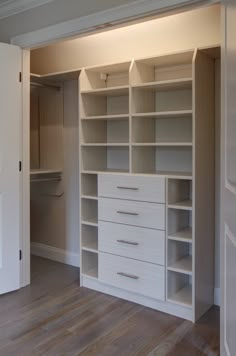 an empty walk in closet with white shelves and drawers