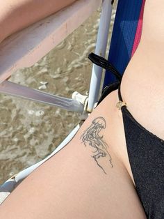 a woman with a tattoo on her stomach sitting next to a beach chair and looking at the water