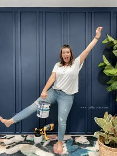 a woman holding a paint can in the air while standing next to a potted plant