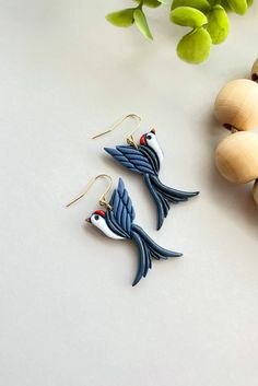 two bird earrings sitting on top of a table next to some beads and flowers,