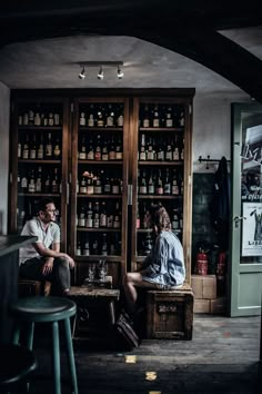 two people sitting at a table in a room with shelves full of bottles and liquor