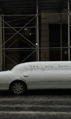 a white car parked in front of a scaffolding with writing on the side