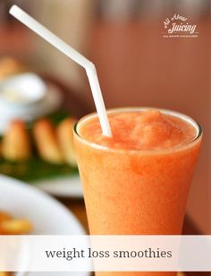 an orange drink with a straw in it sitting on a table next to some food