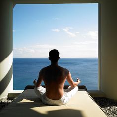 a man sitting on top of a bed in front of an open window looking out at the ocean