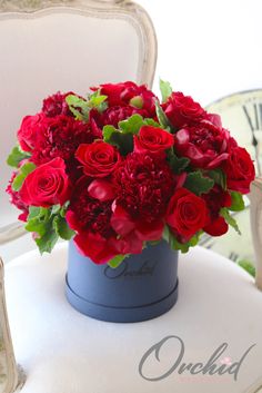 a bouquet of red roses in a blue vase on a white chair with a clock behind it