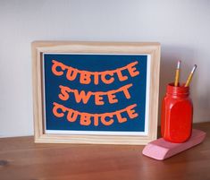 an orange and blue sign sitting on top of a wooden table next to a red pen holder