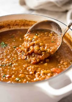 a ladle full of beans being spooned into a white pot filled with soup