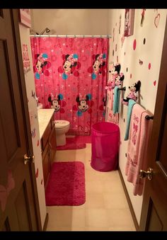 a bathroom decorated in minnie mouse theme with pink rugs and shower curtain, mickey mouse head on the wall