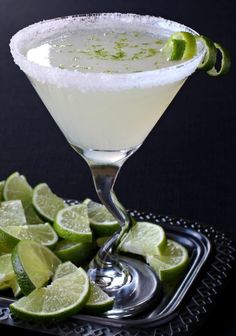 a margarita with limes and sugar on the rim in a martini glass next to sliced limes