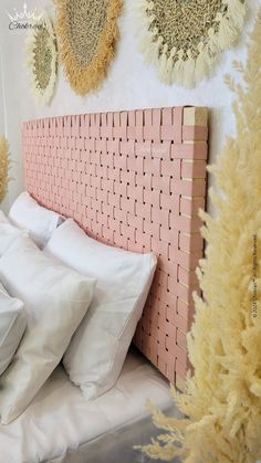 a bed with white pillows and pink headboard next to wall hangings on the wall