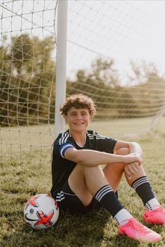 a young man sitting on the ground next to a soccer ball in front of a goal