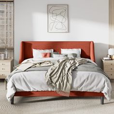 a bed with an orange headboard and white sheets in front of a painting on the wall