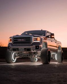 a large truck parked on top of a parking lot next to a field at sunset