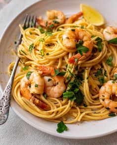 a plate of pasta with shrimp and parsley garnished with lemon wedges