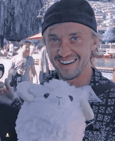 a man holding a stuffed animal in his right hand and smiling at the camera with other people behind him