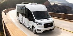 a white bus driving down a road next to mountains