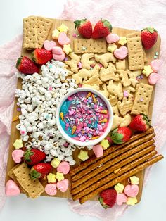 a wooden board topped with crackers, strawberries and marshmallows next to a bowl of cereal