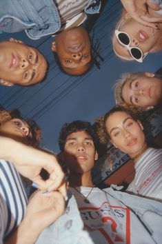 a group of people standing in a circle looking up at the camera with their hands together