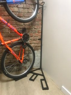 an orange bike hanging on the side of a brick wall next to a bicycle rack