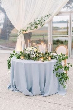 a table with candles and greenery on it in front of an open window at night