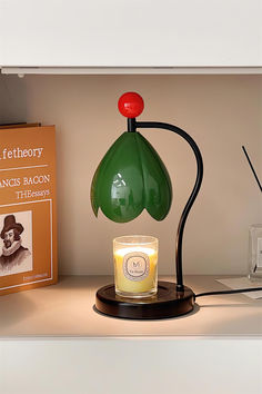 a green glass lamp sitting on top of a table next to a book and candle