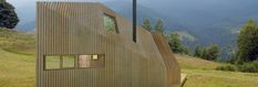 an unusual wooden structure on top of a hill with trees in the background and mountains behind it