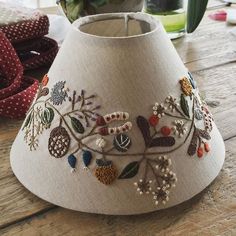 a lamp shade with embroidered flowers on it sitting on a table next to a potted plant