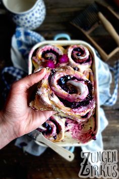 a person holding up a pastry with blueberries and cream in it on a plate