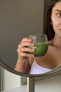 a woman holding a green drink in front of a mirror