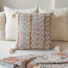 a crocheted pillow with tassels on top of it sitting on a bed