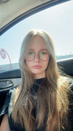 a woman with glasses sitting in the back seat of a car looking at the camera