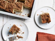 two plates with slices of cake on them next to a pan filled with desserts