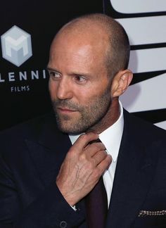 a bald man in a suit adjusts his tie