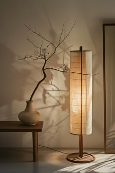 a table lamp sitting next to a vase with a tree branch on it and a mirror in the background