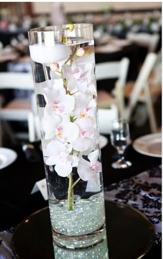 a tall vase filled with white flowers on top of a black table covered in plates and silverware