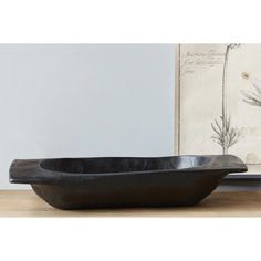 a large black bowl sitting on top of a wooden table next to a framed painting