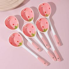 six spoons with strawberry designs on them sitting next to a straw hat and pink background