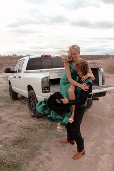 two women in green dresses are carrying a man into the back of a pickup truck