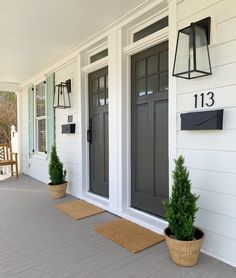 two potted plants on the front porch of a white house with black doors and numbers