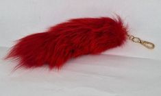 a red furry animal keychain on a white surface with a gold metal hook