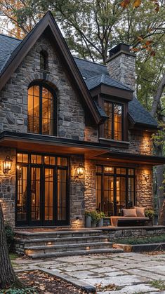 a stone house with large windows and steps leading up to the front door, surrounded by trees